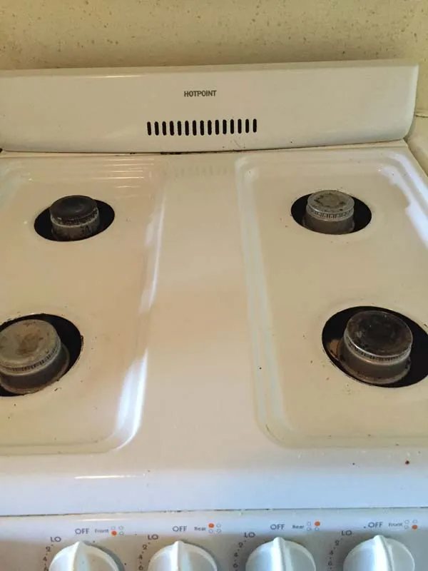 White gas stovetop with four exposed burners and front control knobs