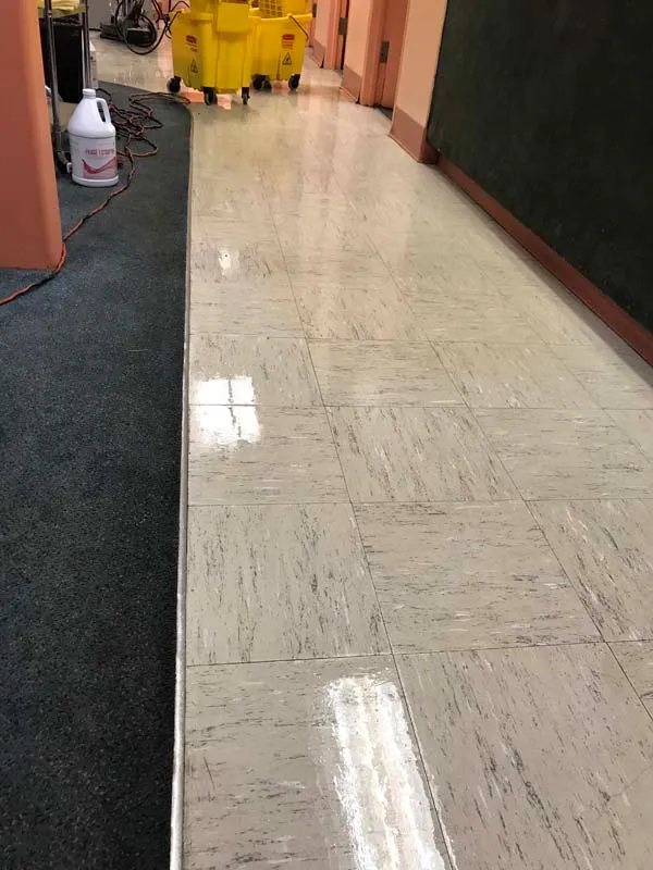 Polished hallway tile reflecting light beside carpet and floor-cleaning equipment