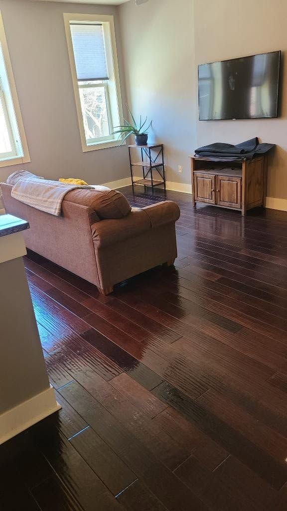 Dark hardwood flooring in a furnished living room with a brown sofa and wall-mounted television