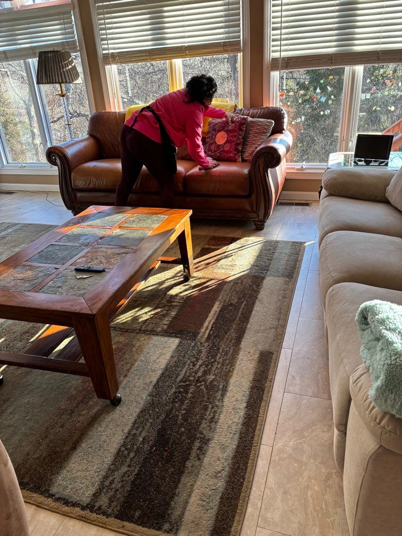 American Maids team member arranging cushions on a brown sofa in a sunlit living room