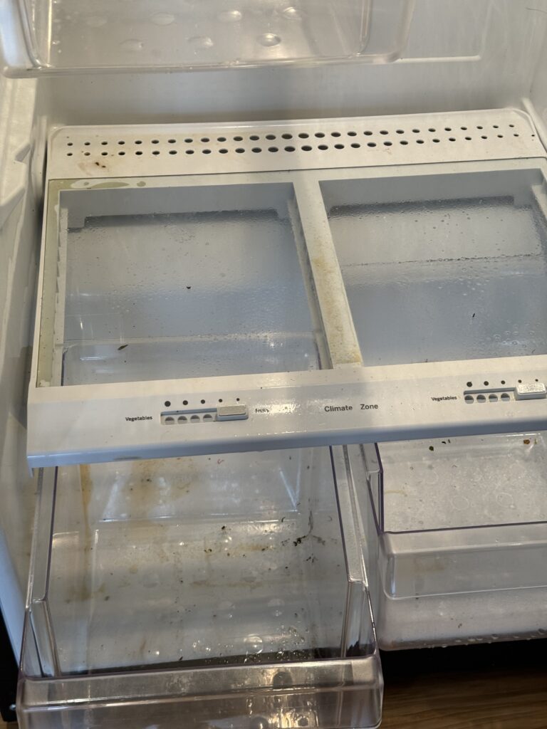 Close-up of a dirty fridge interior with stained drawers before being cleaned by American Maids.