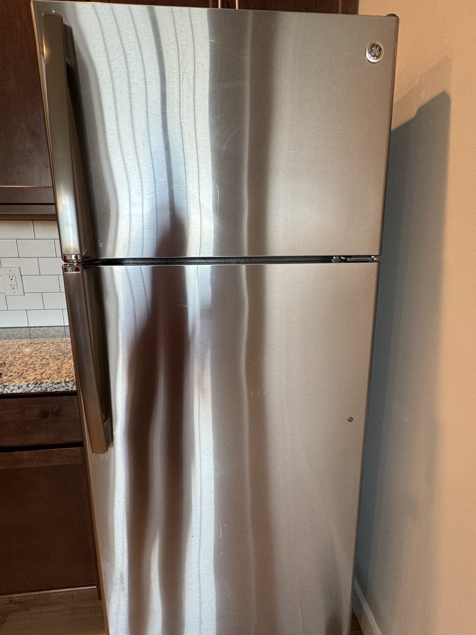 A stainless steel fridge with visible streaks and smudges before cleaning by American Maids & Floor Cleaning Specialist.